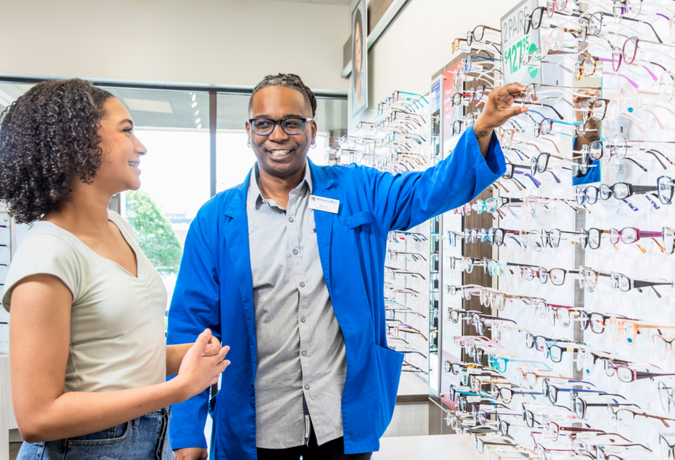 Smiling female African American National Vision employee helping a customer pick out new frames.